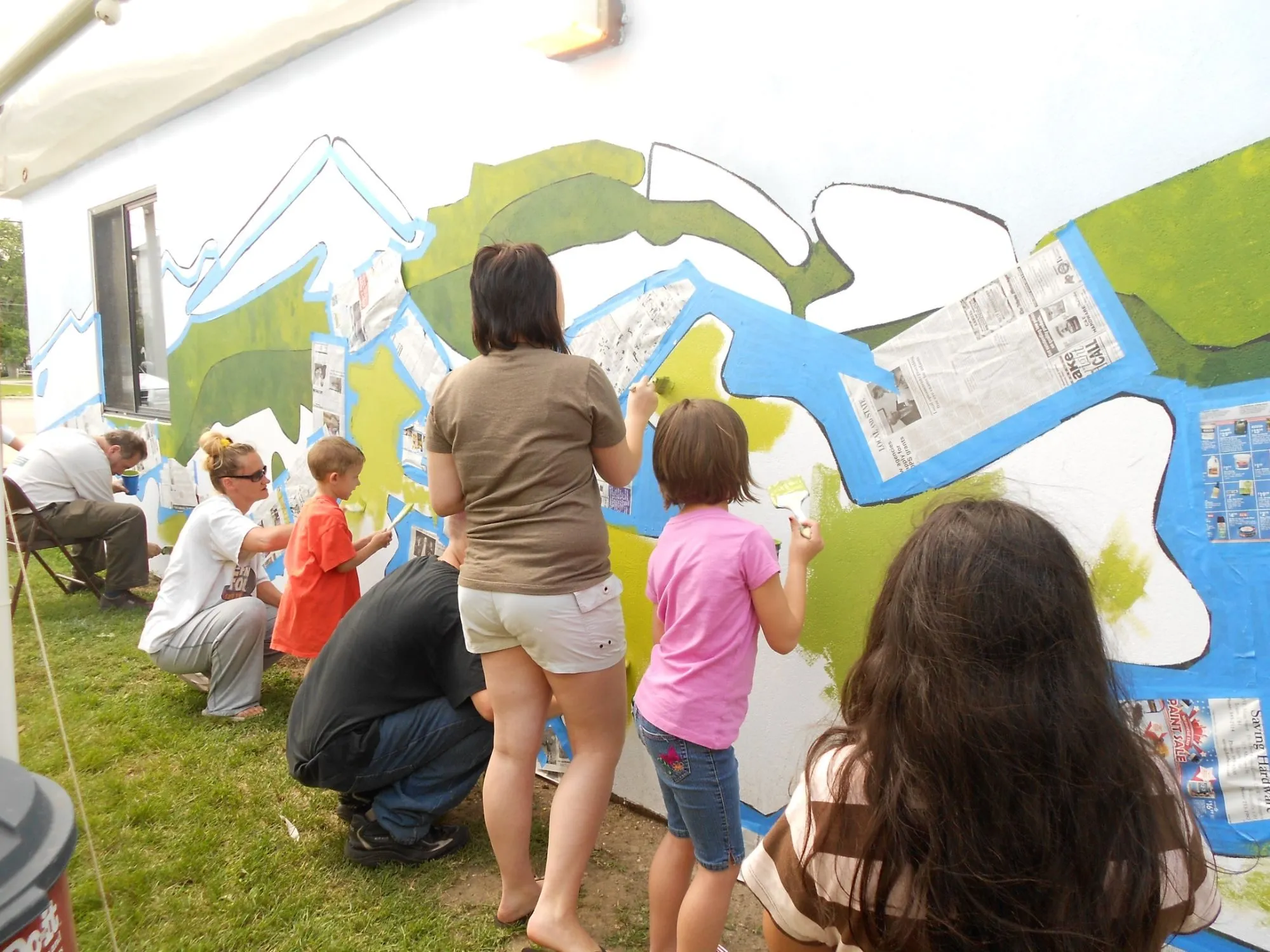 Volunteers of all ages filling in the hills with brushes, the shapes masked off with tape and newspaper