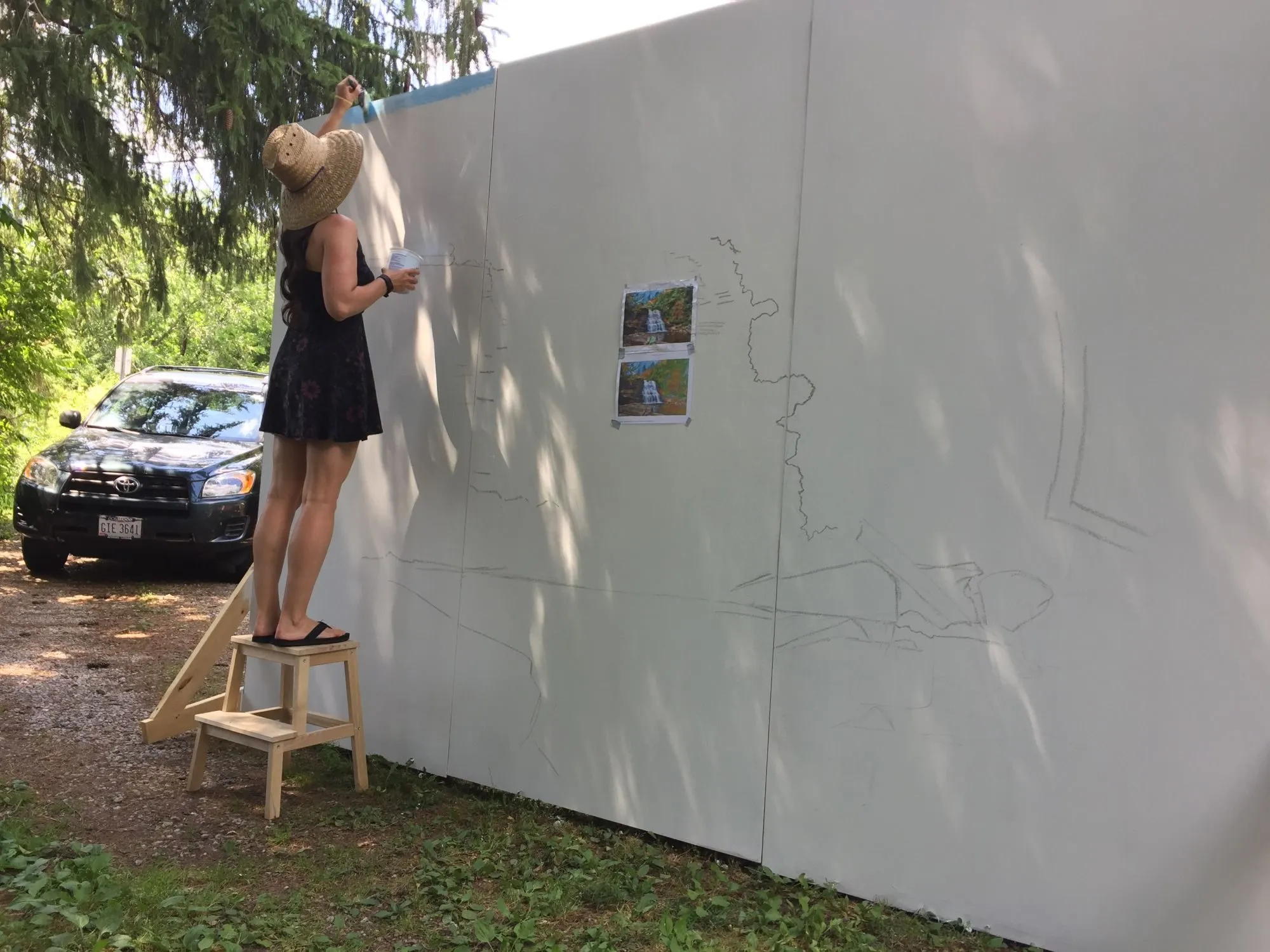 Kasey on a step stool painting in the sky at the top of the mural, the rest of the falls still sketched in pencil