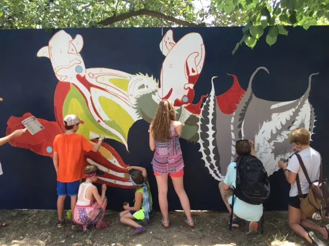 Children and adults filling in the outlined shapes along the mural wall