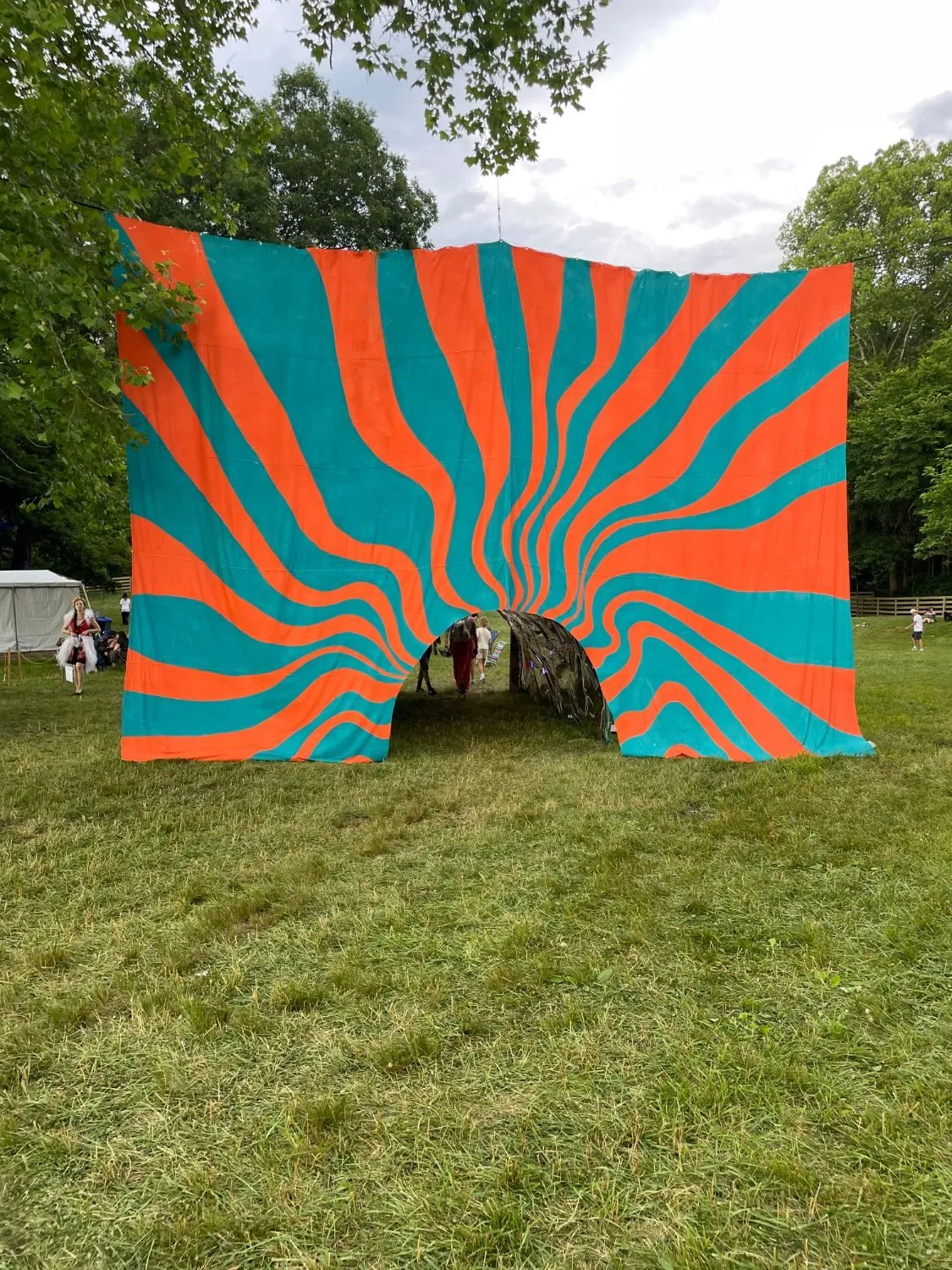 The full installation seen head on, the orange and teal sunburst backdrop with the mirrored tunnel open at its center