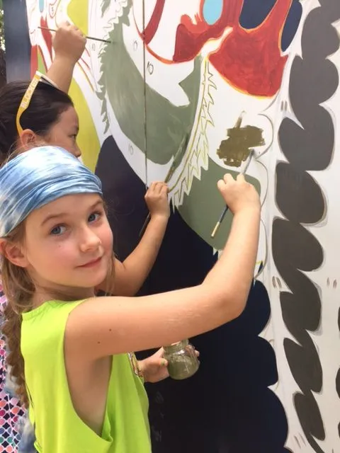 A girl in a blue bandana painting one of the shapes, brush in hand