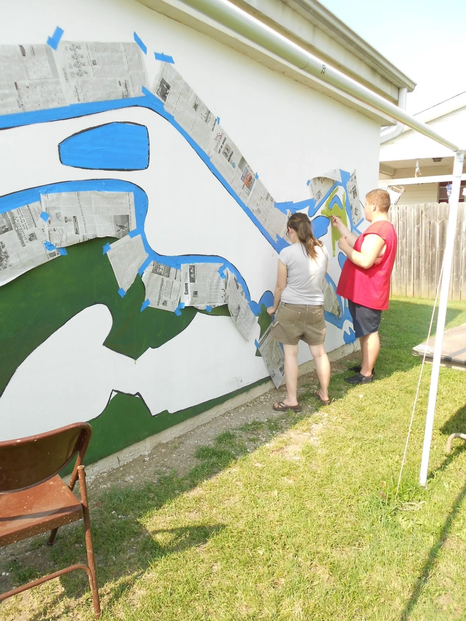 Two volunteers painting along the taped edge at the end of the wall