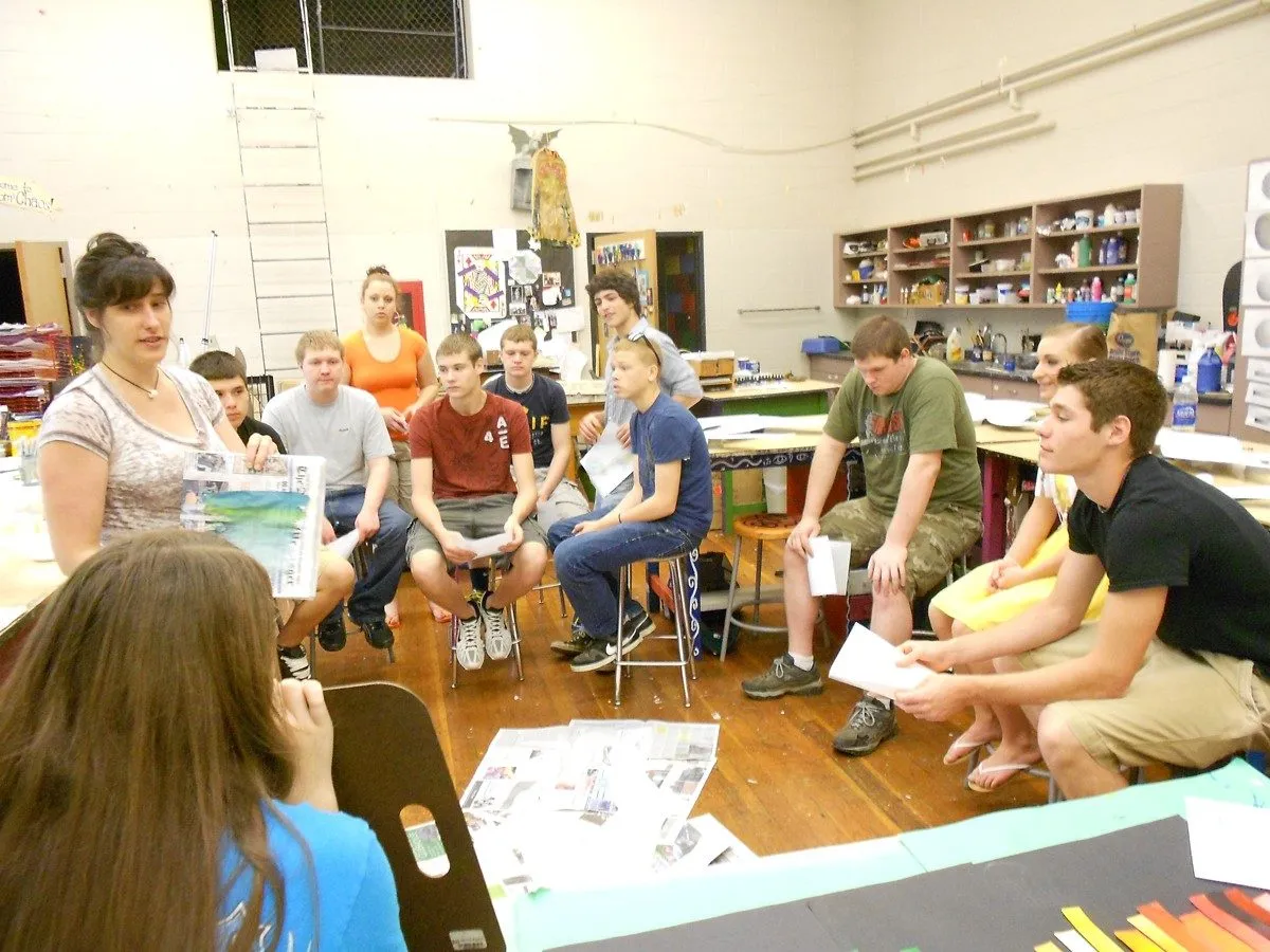 A group gathered in a circle in the art room, studies in hand