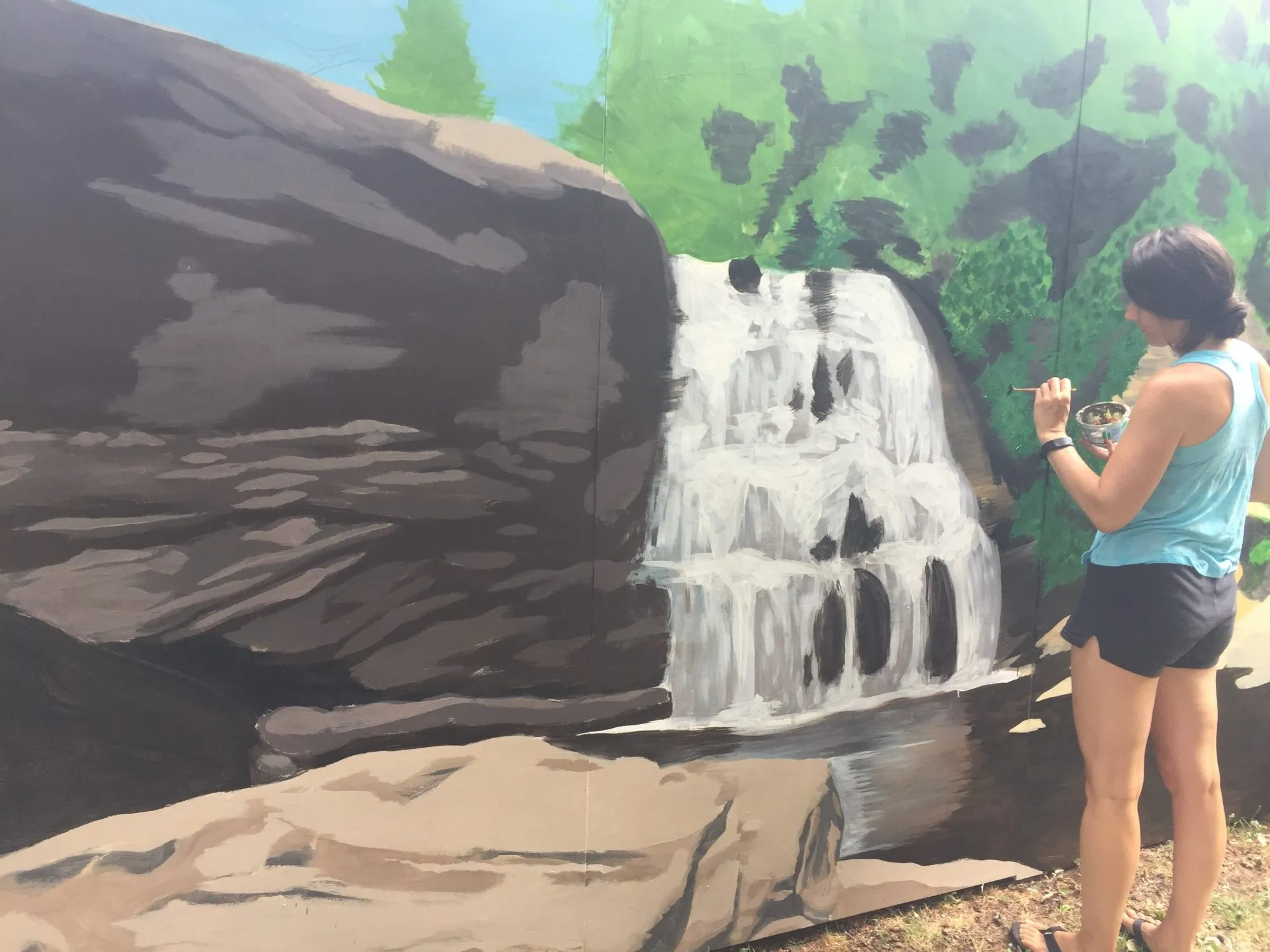 Kasey working on the falling water with a small brush and a cup of paint