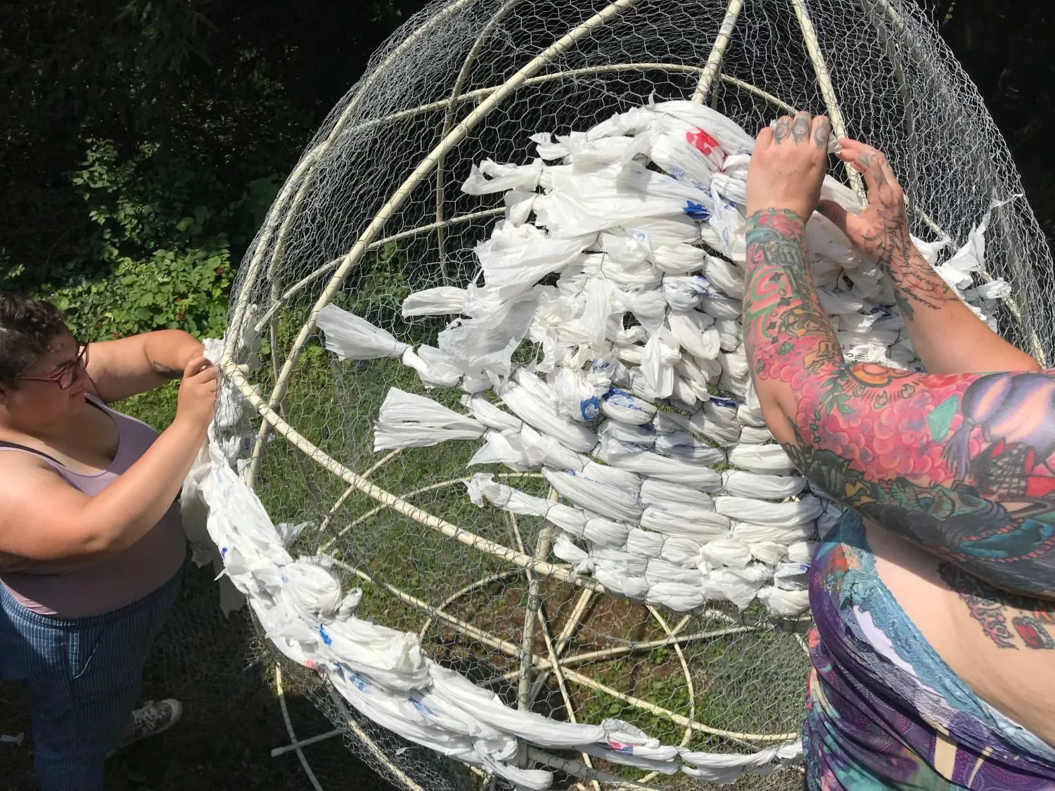 Two of the team weaving plastic bags onto the chicken wire and PVC frame of the head