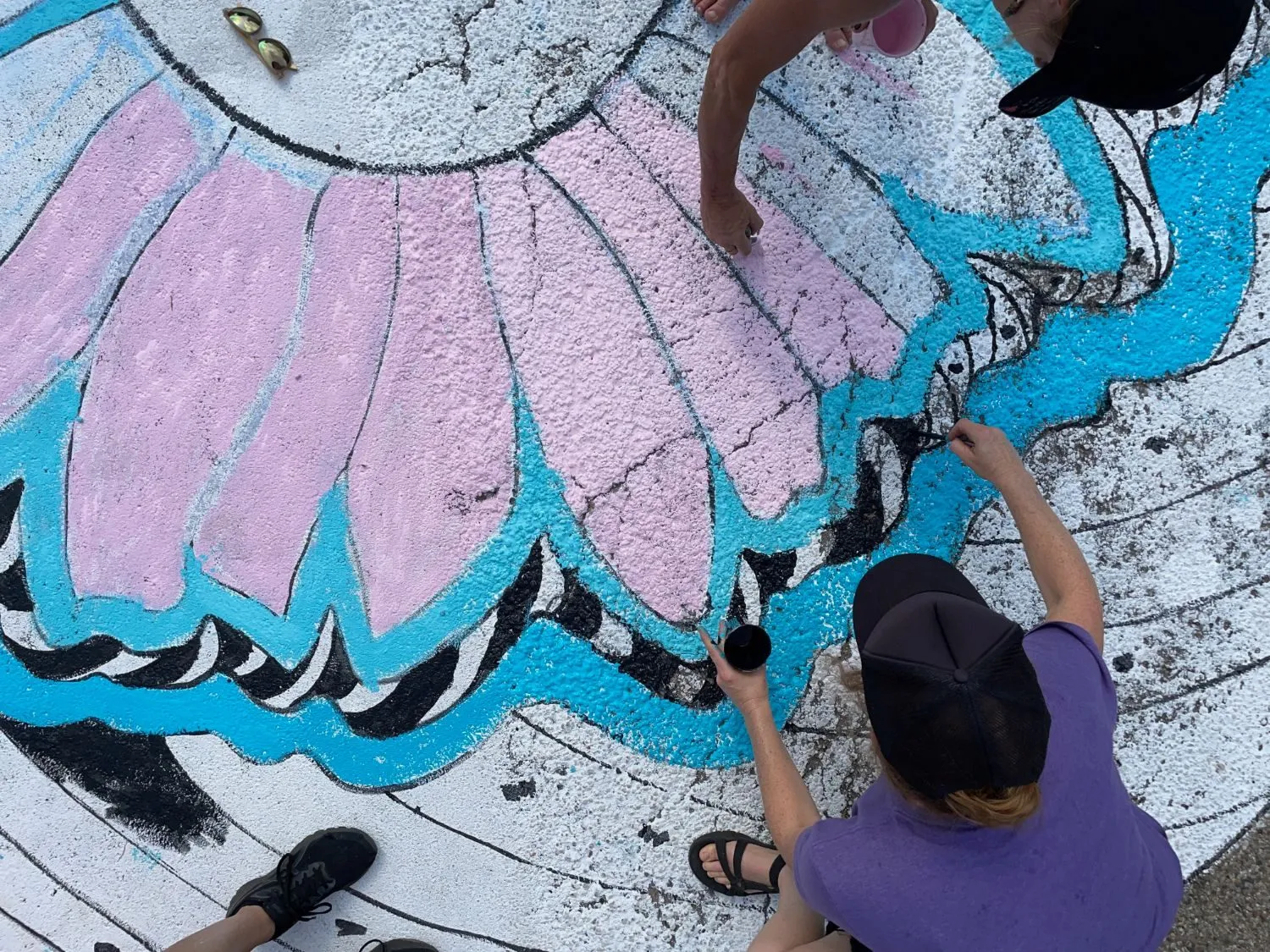 Overhead view of two people kneeling on the street painting the black outlines of the pink coneflower petals