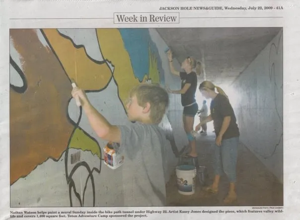 A newspaper clipping showing three young volunteers painting inside the tunnel, one of them filling in a large shape with a roller