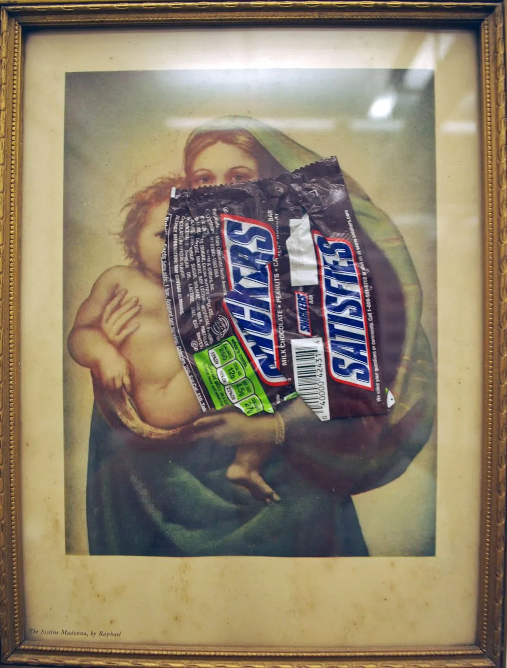 A framed devotional print of the Madonna and child, a Snickers wrapper collaged across the mother's arm and shoulder