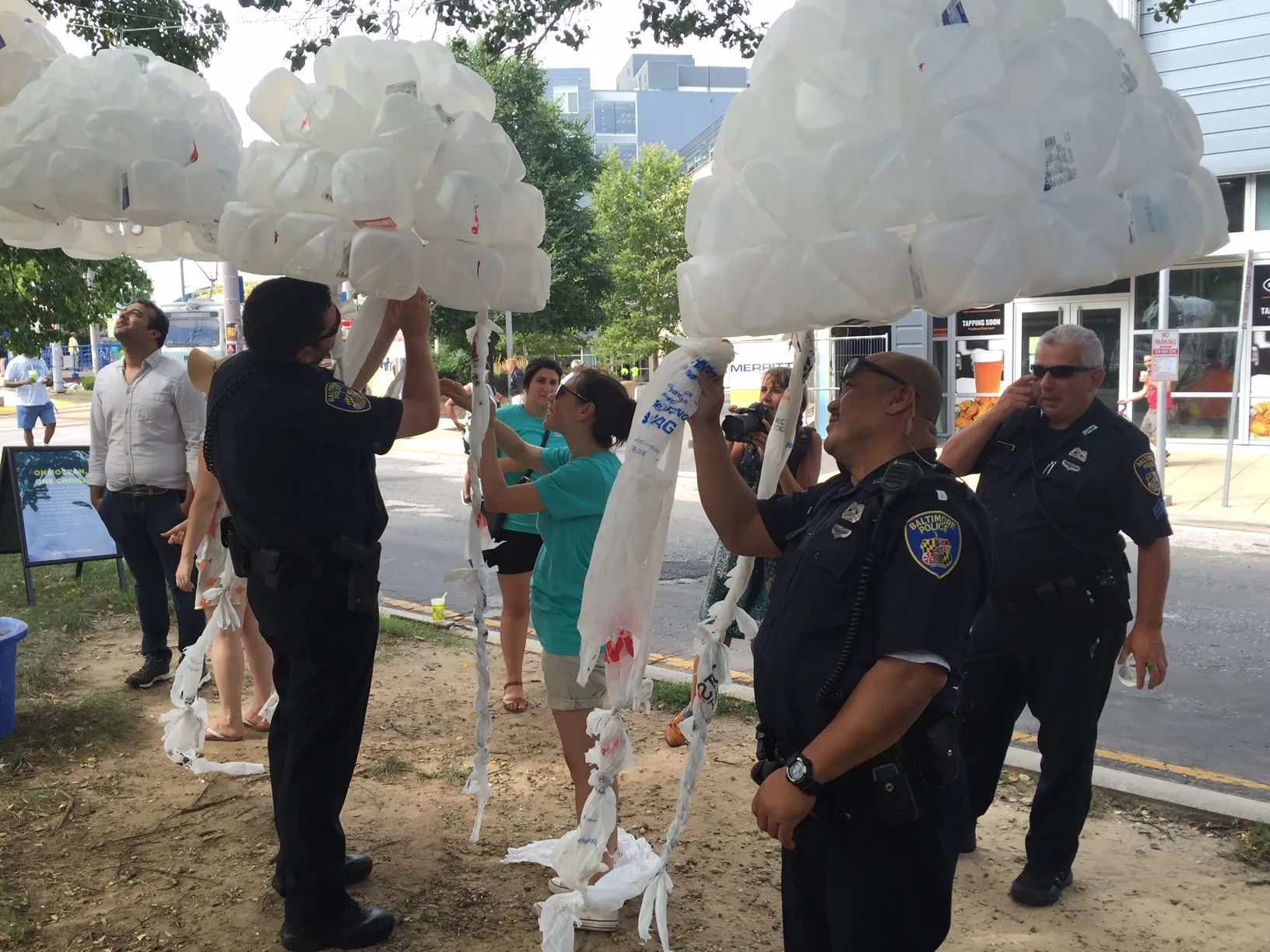 Festival goers and Baltimore police officers helping tie plastic bag tentacles onto a bell
