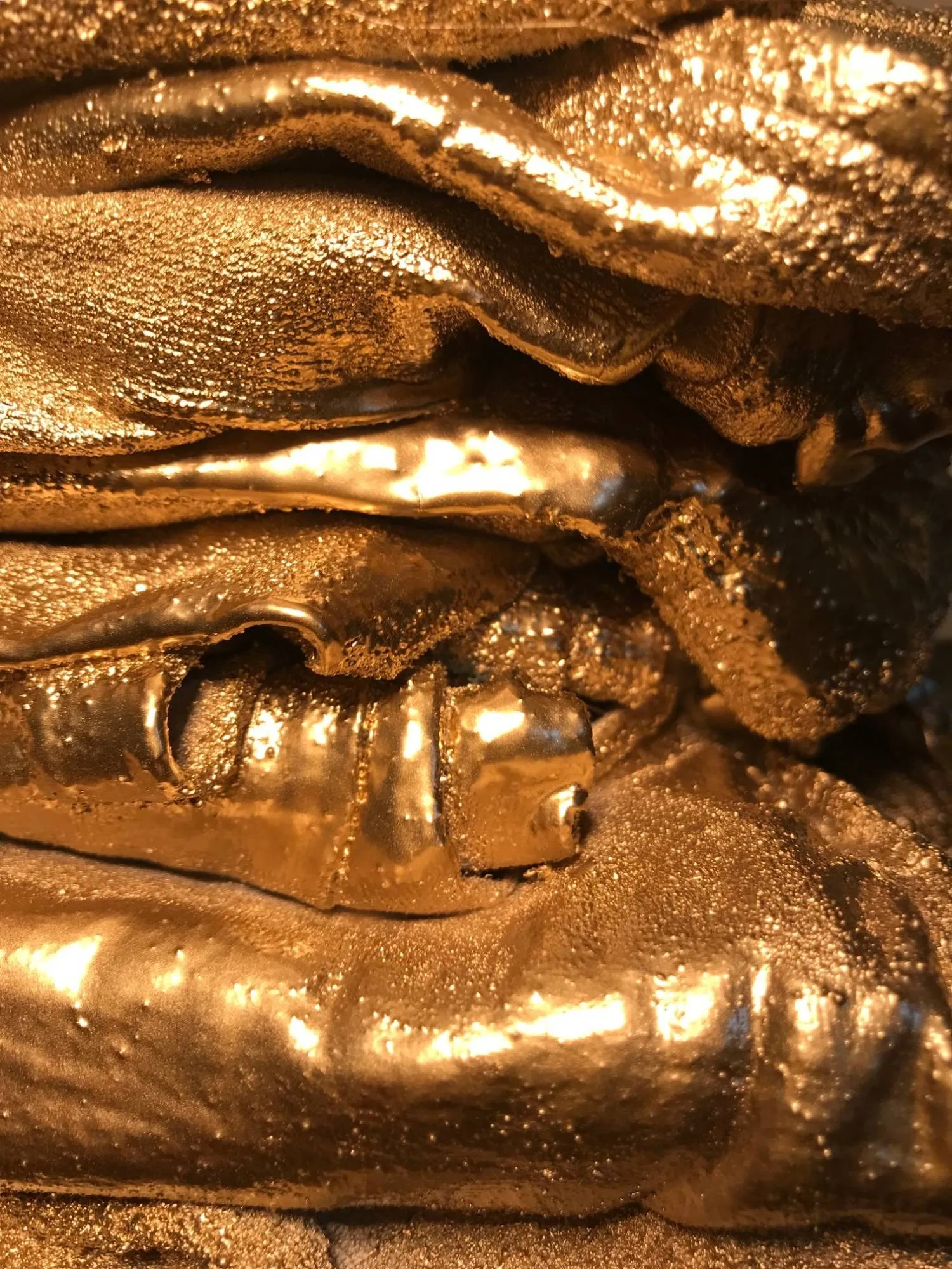 Closer still, the gold paint pooling in the creases and catching the light along a folded edge