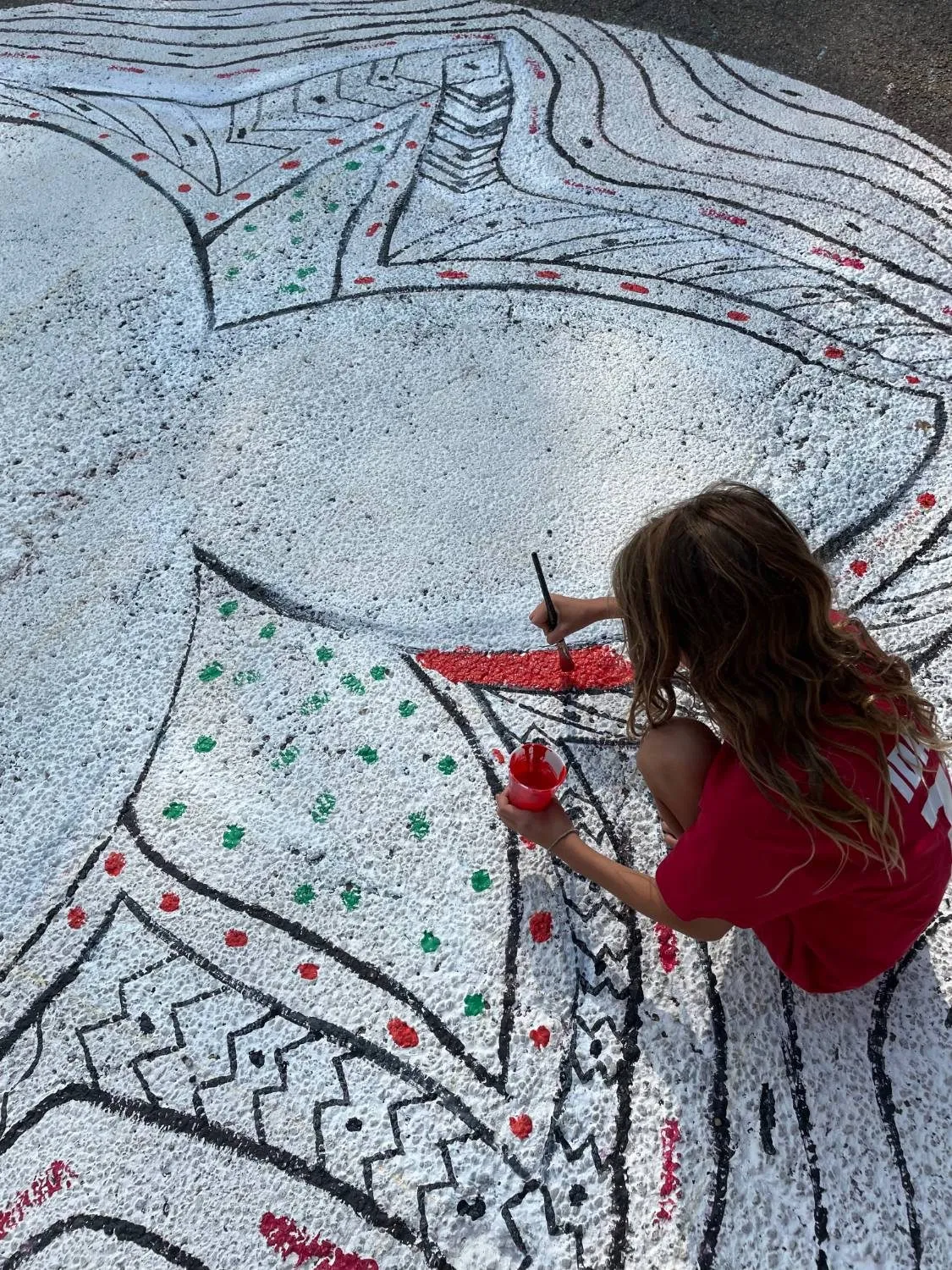 A woman crouched on the white-primed trillium mural, brushing red paint along one of the outlines