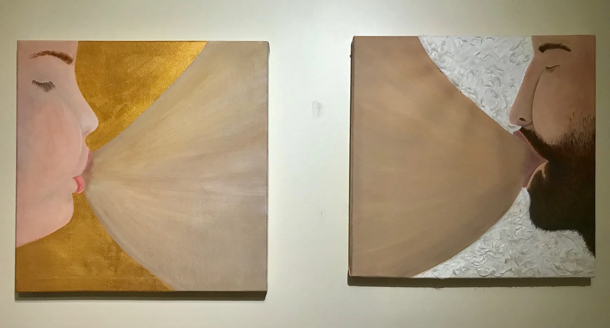 Two square canvases hung side by side, each a face in profile with eyes closed and mouth to a pale breast: a woman against gold on the left, a bearded man against white on the right