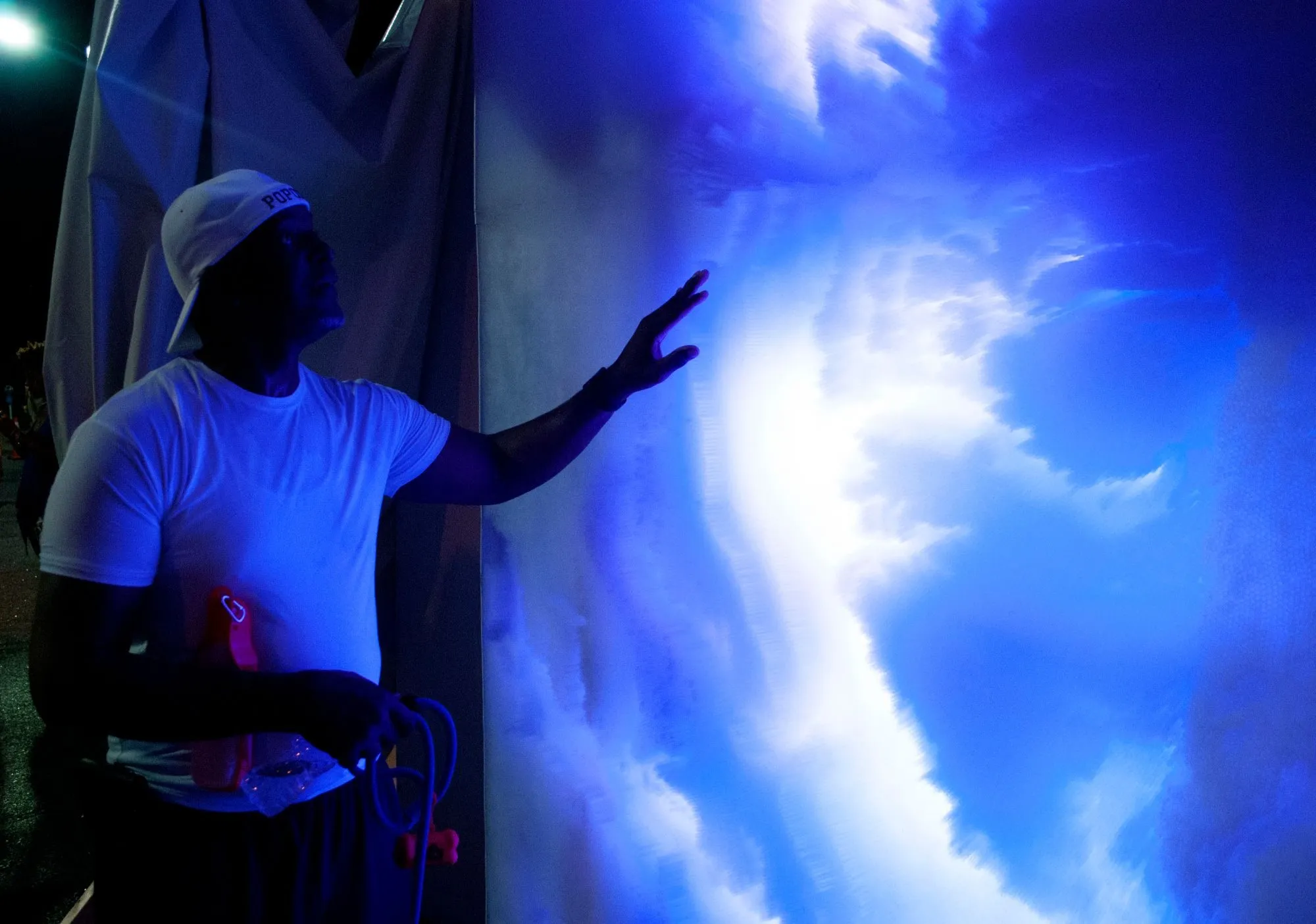 A man in a white cap reaching out to touch the piece, lit deep blue in the dark