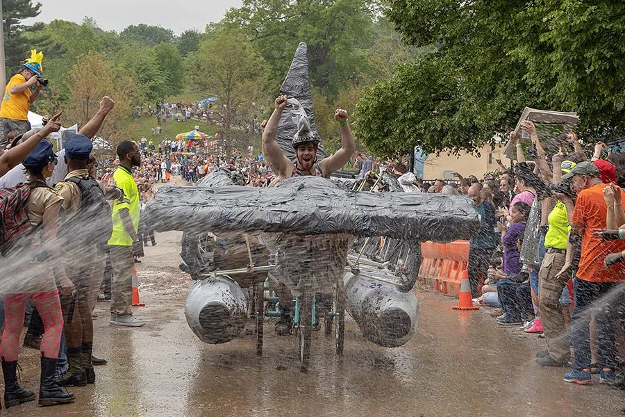 Cresting the mud hill, the rider's arms up and the crowd cheering