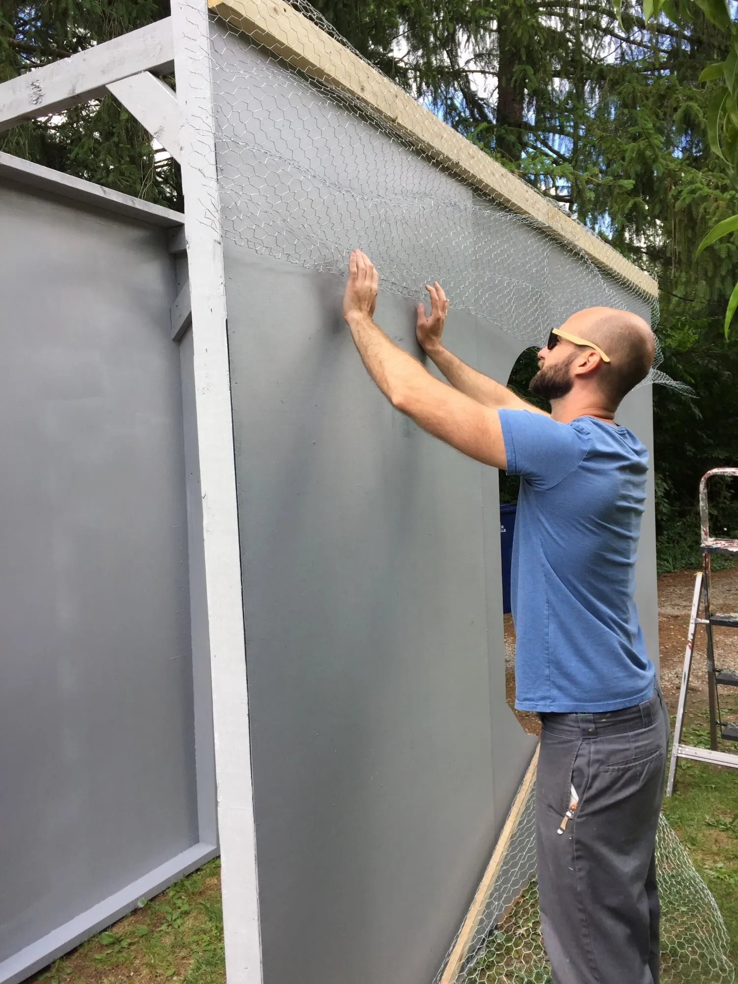 A volunteer stapling chicken wire along the top of a grey-painted panel