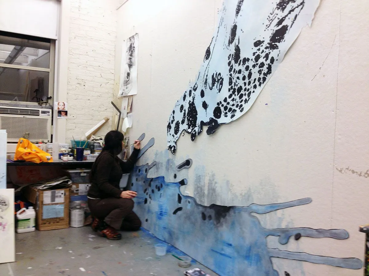 At work in the studio, kneeling to paint a large blue and black form running down the wall