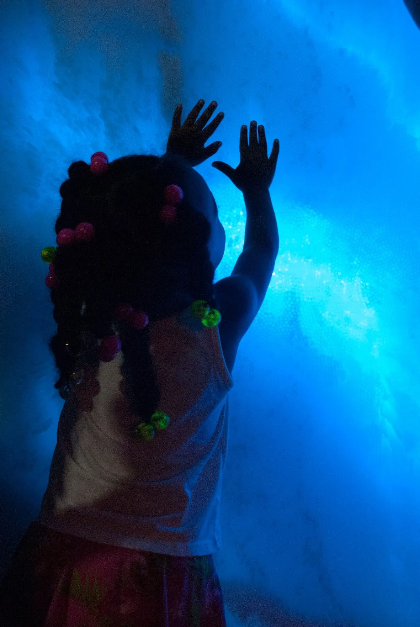 A small girl with beaded braids pressing both hands against the glowing blue surface