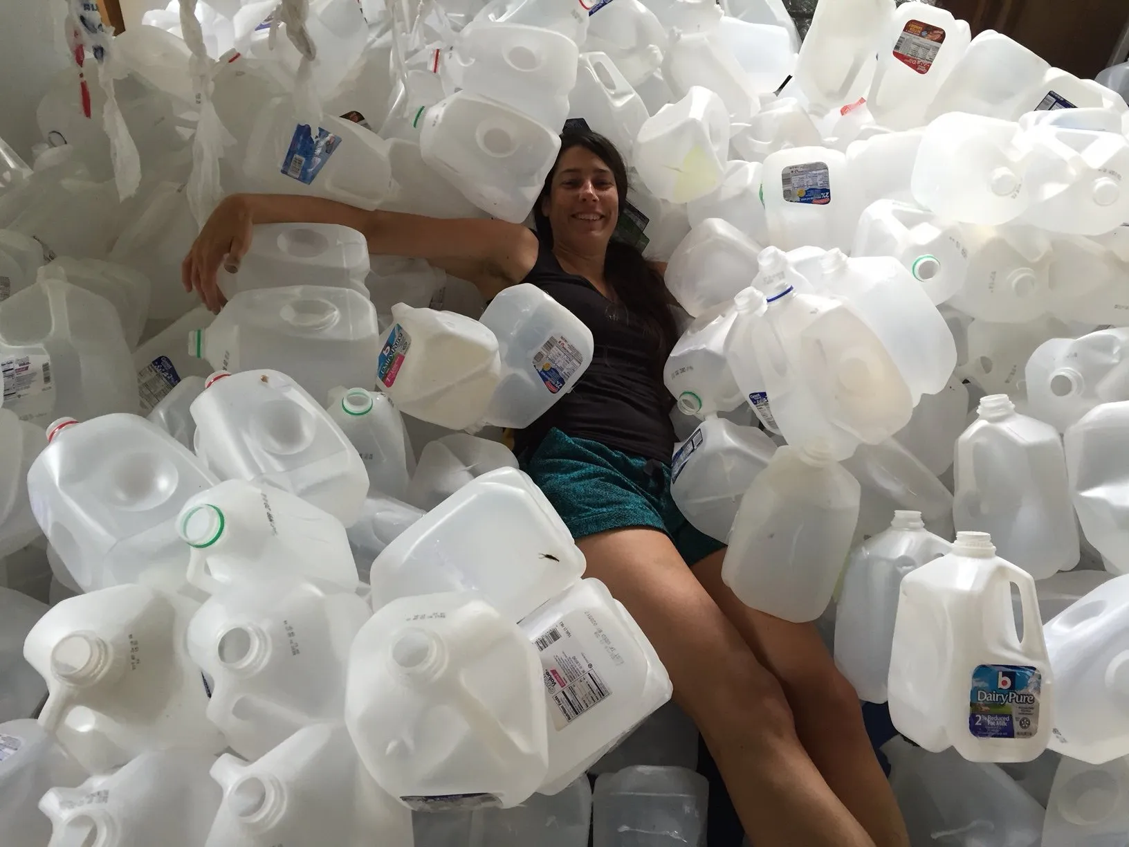 Kasey Jones lying back in a deep pile of empty gallon jugs, grinning up at the camera