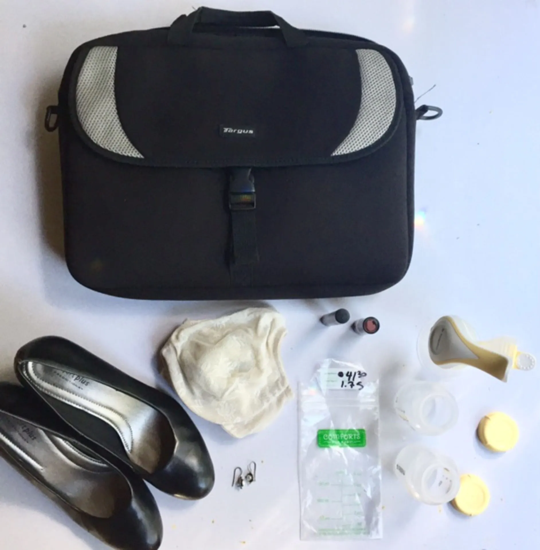 The briefcase, black heels, pearl earrings, nursing pad, pump parts and a labelled milk bag, laid out together