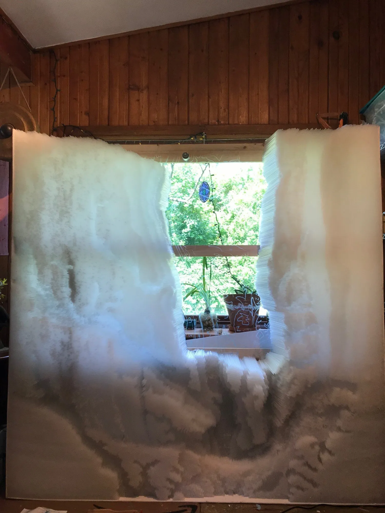 The panel propped in the studio window, the straw surface glowing against the trees outside