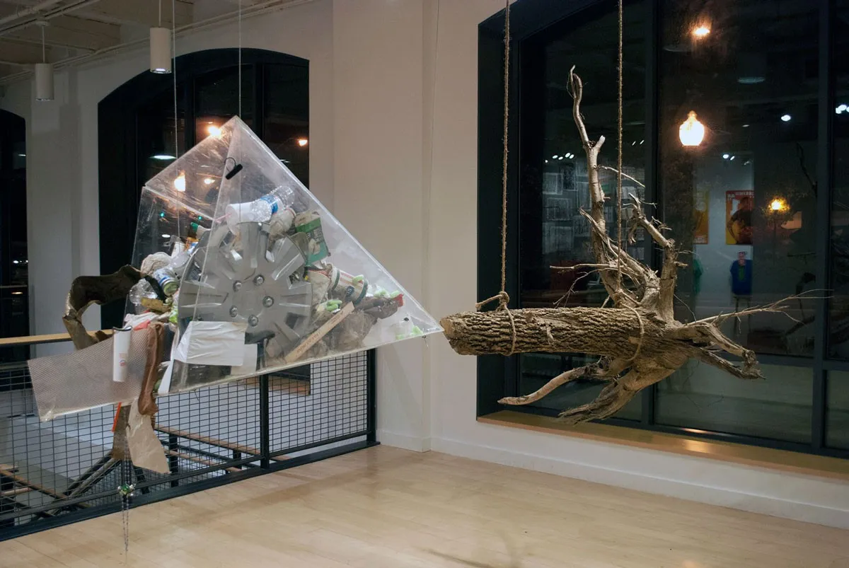 The suspended pyramid of gathered waste at the left of the gallery and the great hanging log facing it across the room