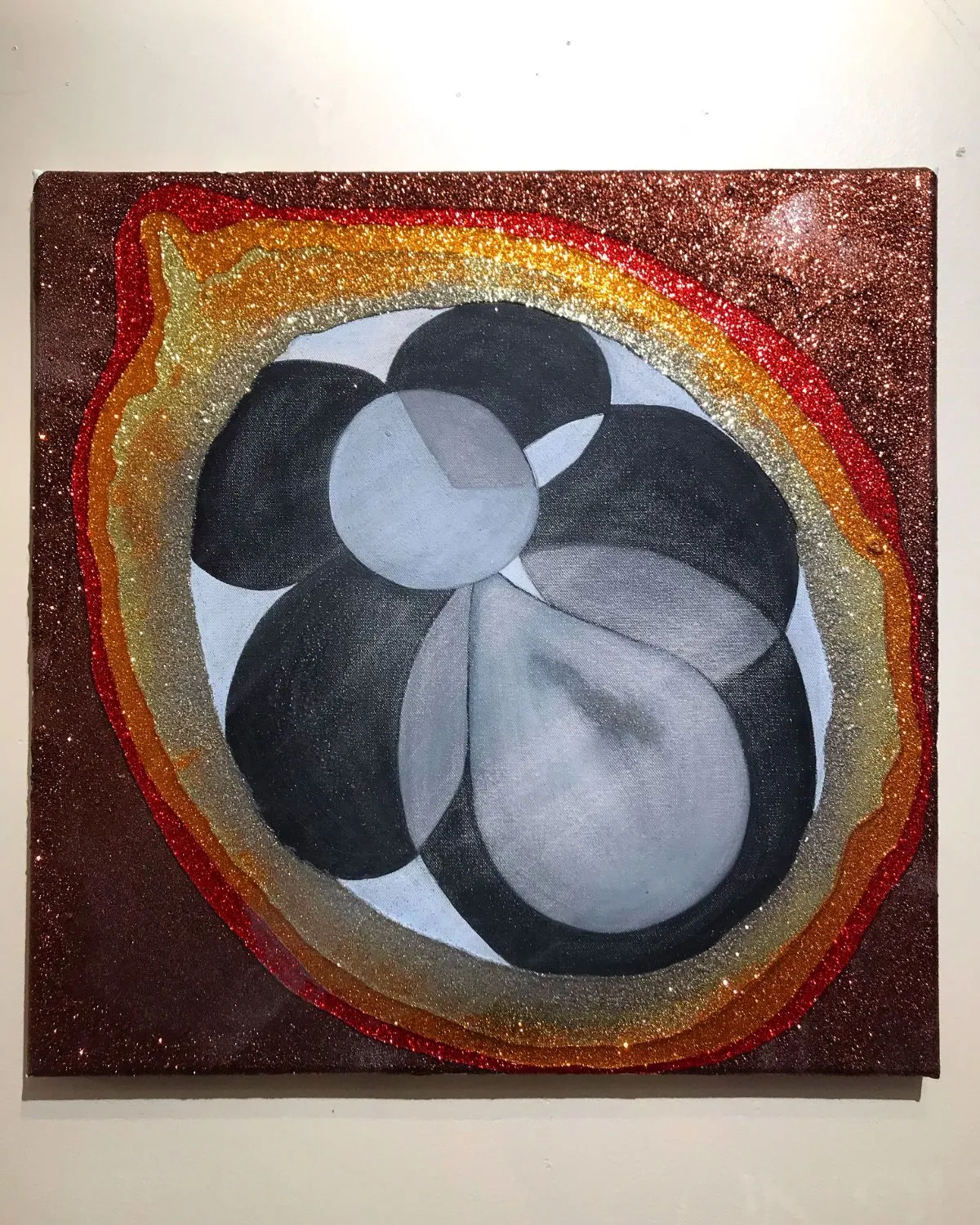 One of the two panels on the wall, the grey forms ringed by bands of red, gold and silver glitter