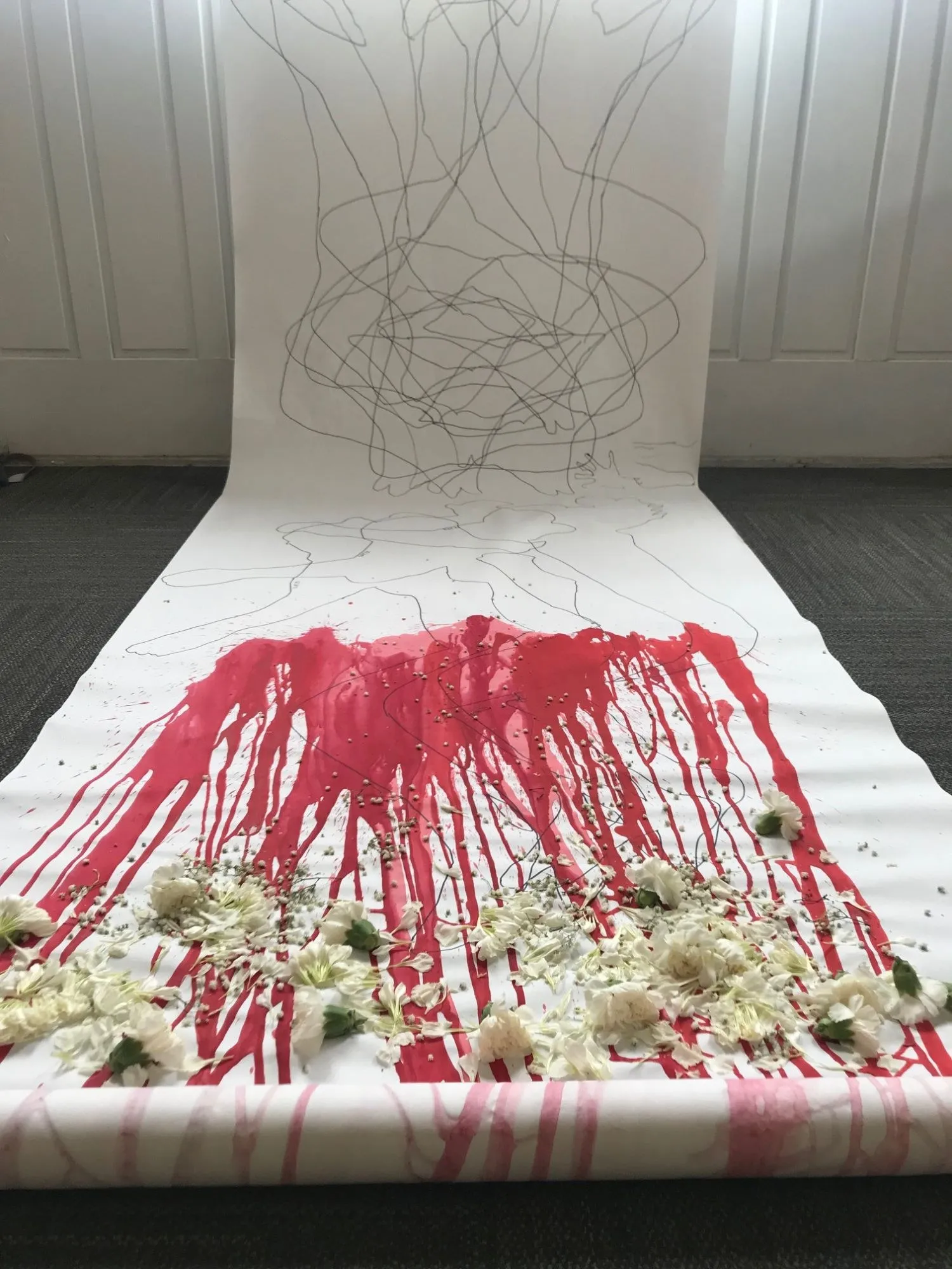 The scroll running down the wall and out across the carpet, the contour drawings above the red and the flowers laid across its foot