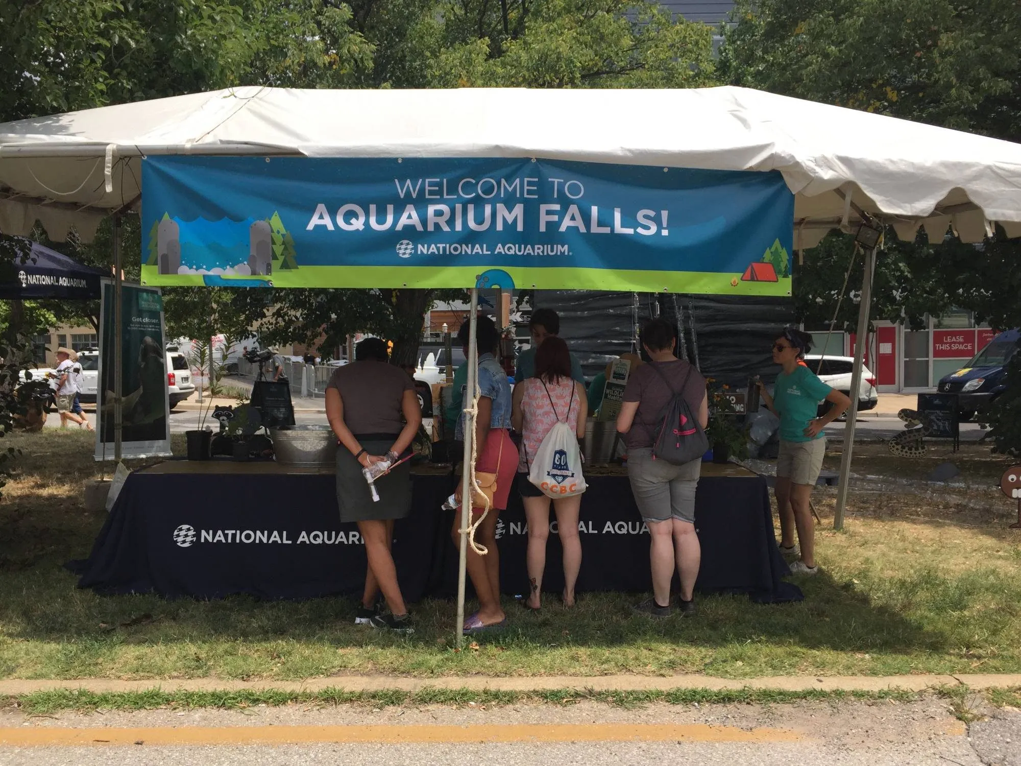The National Aquarium's welcome tent at the festival, visitors gathered at the table beneath the Aquarium Falls banner