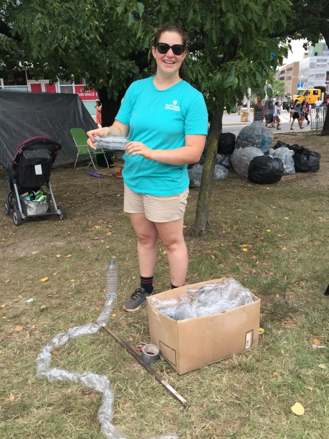 A National Aquarium volunteer holding up a bottle threaded onto the line, bagged bottles stacked behind her