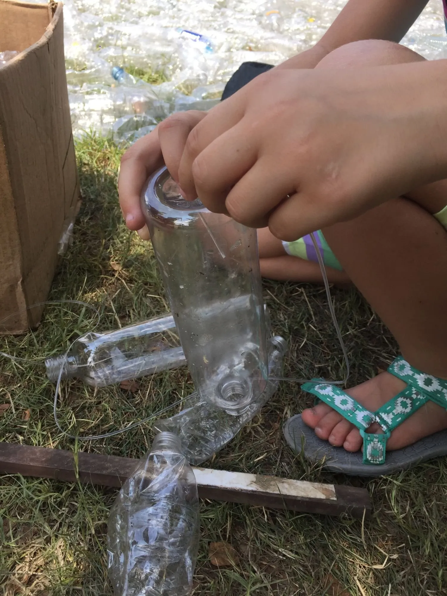 A child's hands feeding a bottle onto the strand, cut bottles waiting in the grass