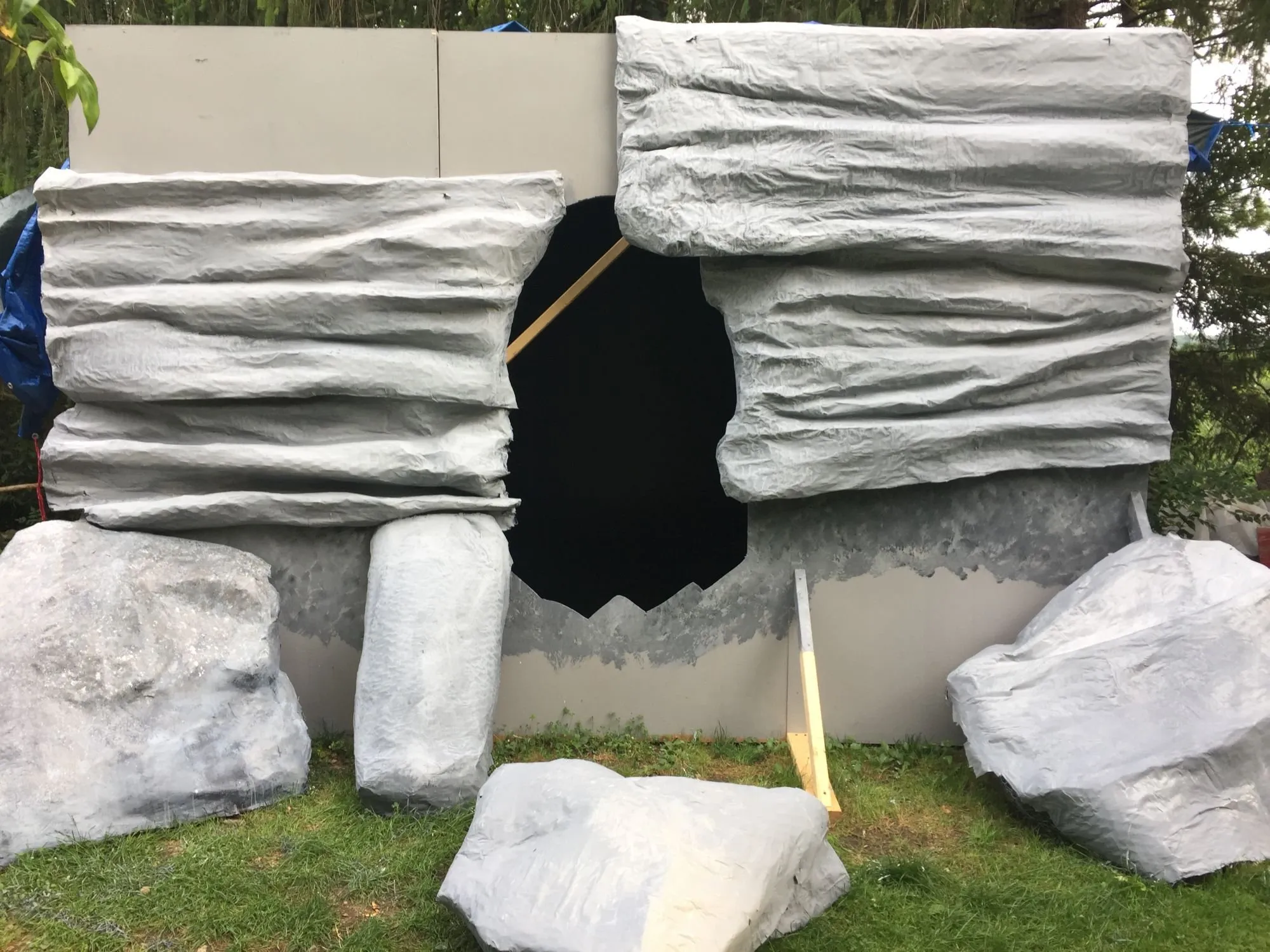 The unpainted facade standing on the grass, the cave opening cut through it and boulders set around its foot
