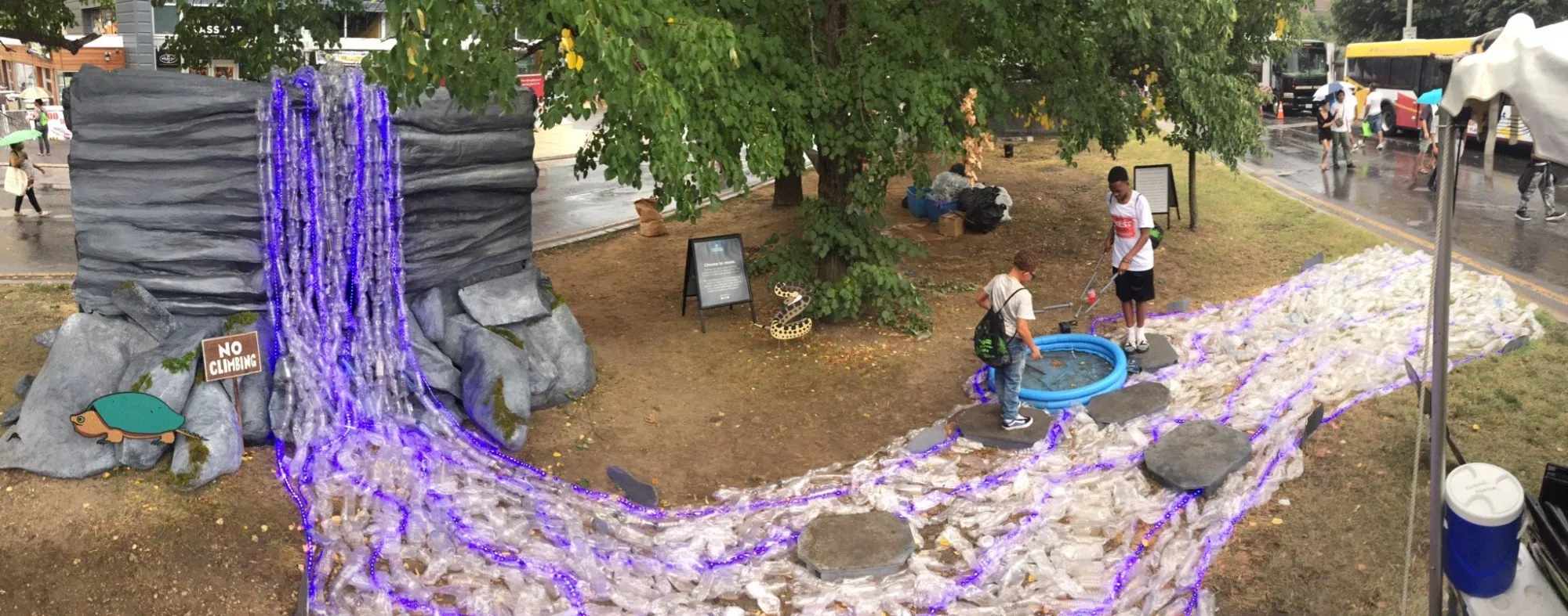 The installation in the rain, the lit falls and bottle stream running between the trees as visitors pass with umbrellas