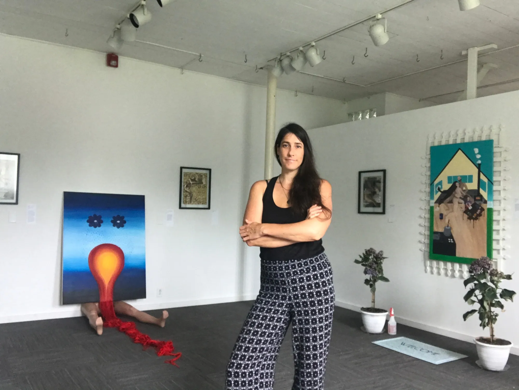 Kasey Jones standing arms folded in the middle of her gallery show, her paintings hung on the walls around her