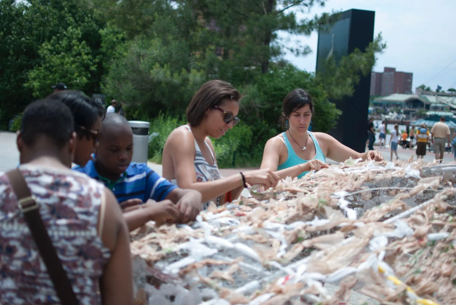 Kasey Jones and visitors weaving strips of plastic bag into a sculpture on the Inner Harbor promenade