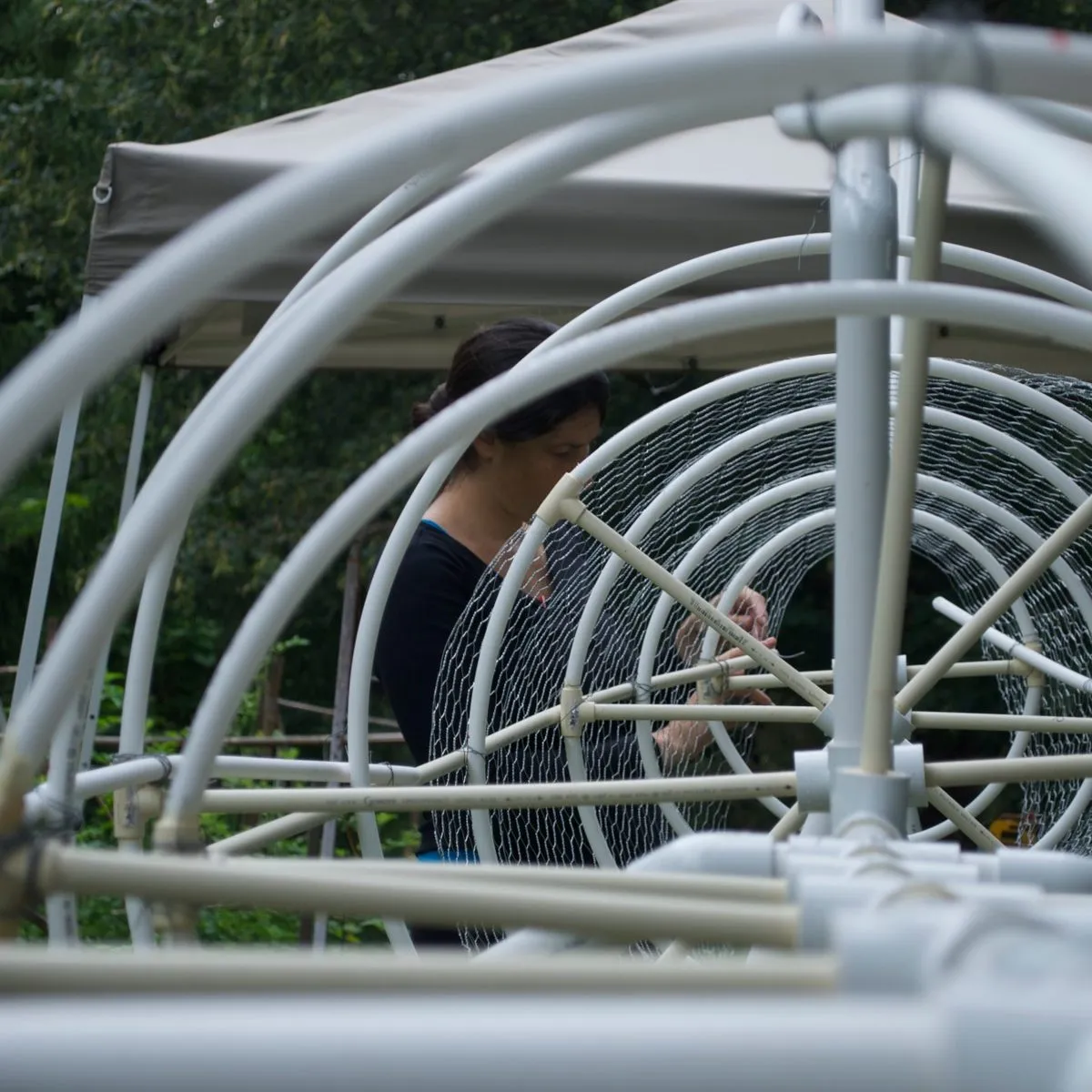 Kasey wiring the pipe frame of the hammerhead shark, rolls of chicken wire behind her