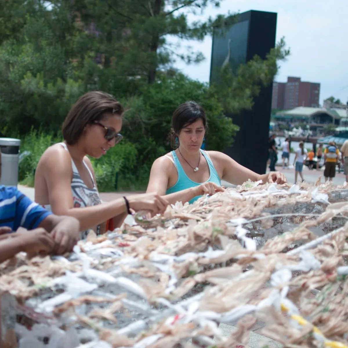 Kasey and visitors weaving plastic bags into a sculpture at the Inner Harbor